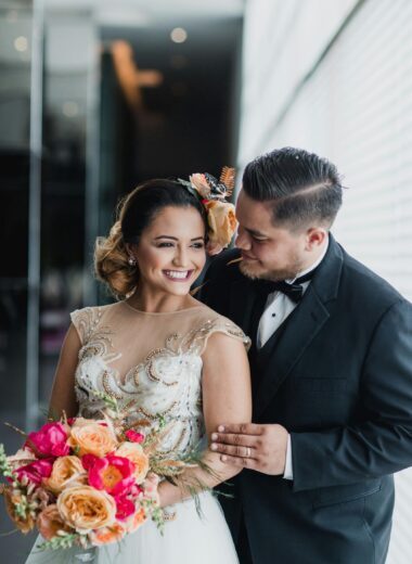 Joyful wedding portrait of a young couple indoors, holding a vibrant bouquet.