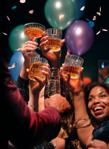 Group of friends raising glasses in a joyful toast, celebrating with balloons and confetti.